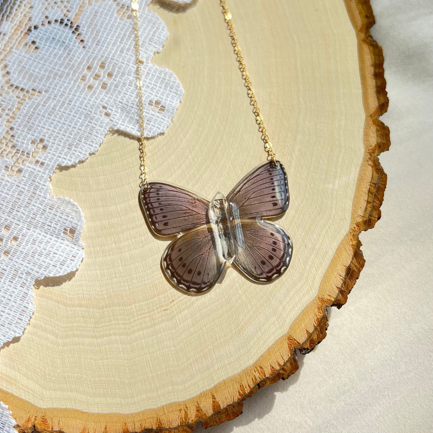 small purple iridescent butterfly necklace with gold chain laying on wooden board