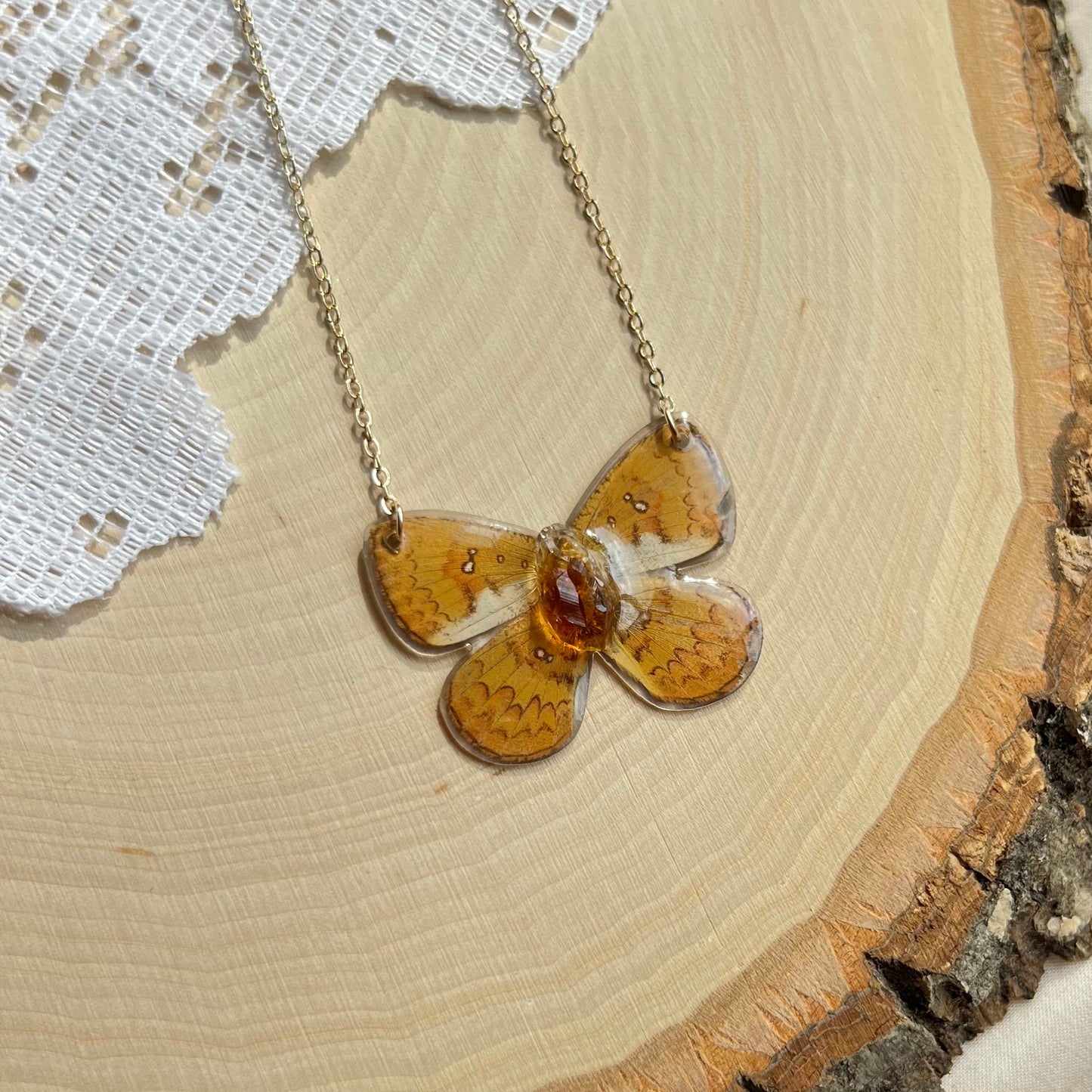 small yellow butterfly necklace with gold chain laying on wooden board