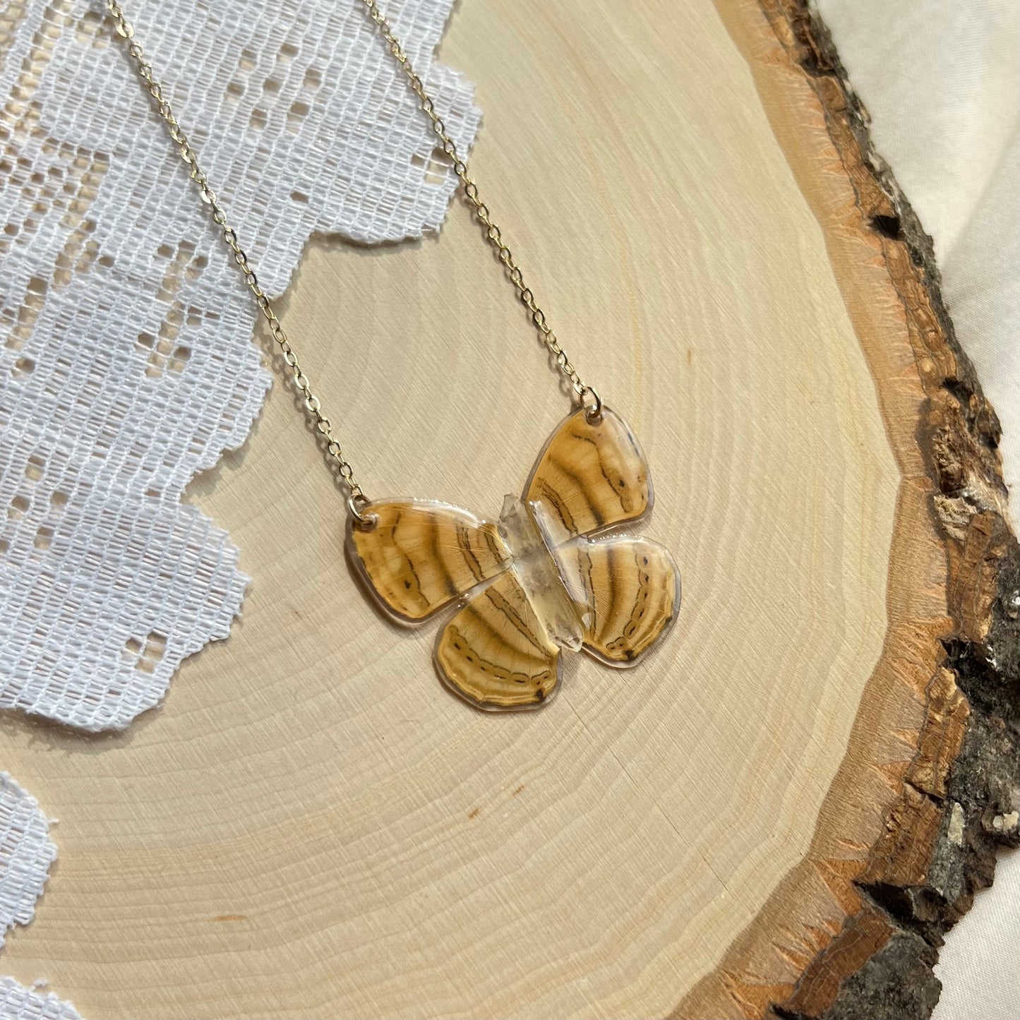 small yellow butterfly necklace with gold chain laying on wooden board