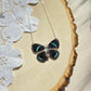 small iridescent blue and black butterfly necklace with sterling silver chain laying on wooden board