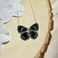 small iridescent blue and black butterfly necklace with sterling silver chain laying on wooden board