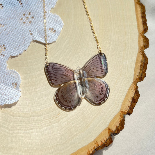 small purple iridescent butterfly necklace with gold chain laying on wooden board