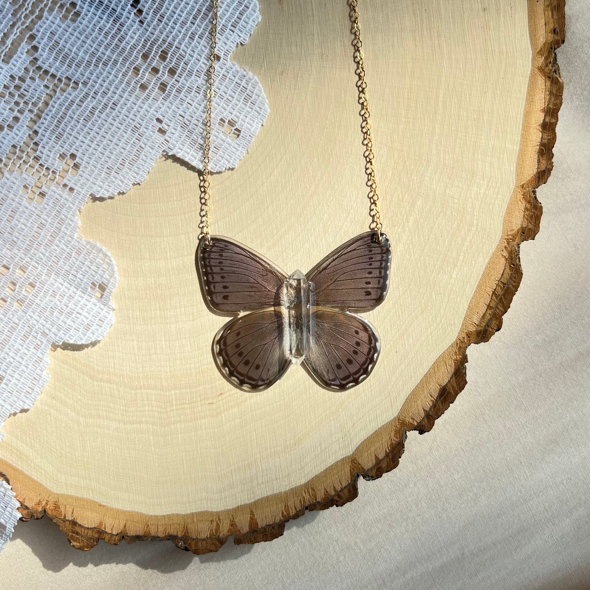 small purple iridescent butterfly necklace with gold chain laying on wooden board