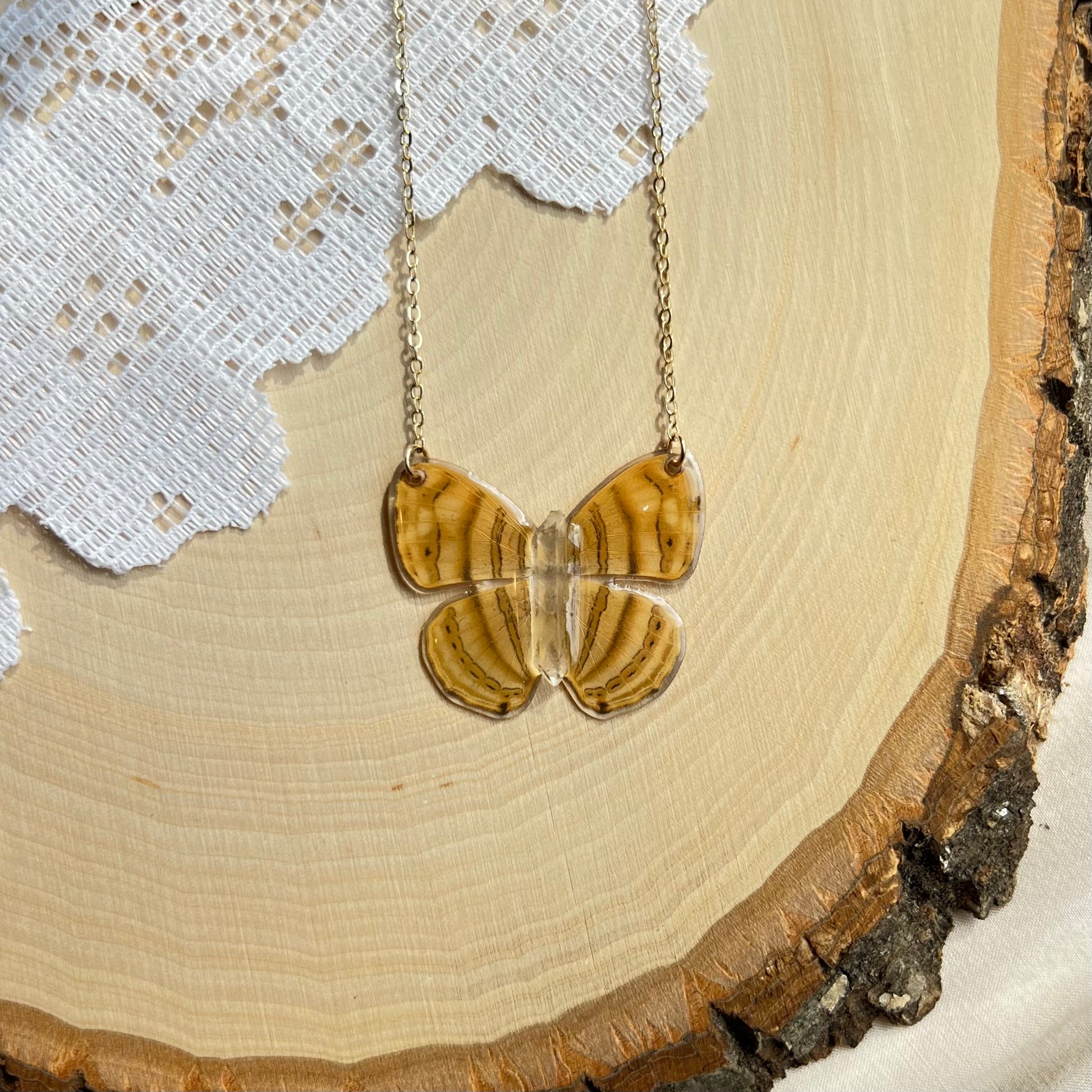 small yellow butterfly necklace with gold chain laying on wooden board